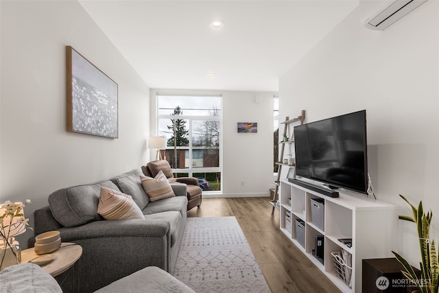 living room with an AC wall unit, plenty of natural light, baseboards, and wood finished floors