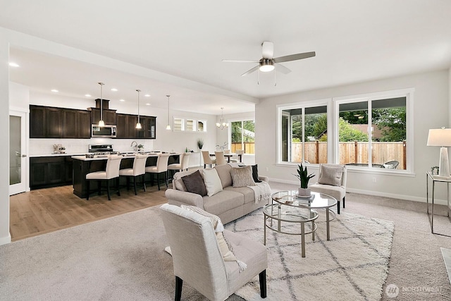 living area featuring ceiling fan with notable chandelier, light wood-style floors, baseboards, and recessed lighting