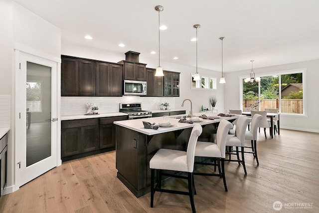 kitchen featuring a breakfast bar area, tasteful backsplash, light countertops, appliances with stainless steel finishes, and light wood-style floors