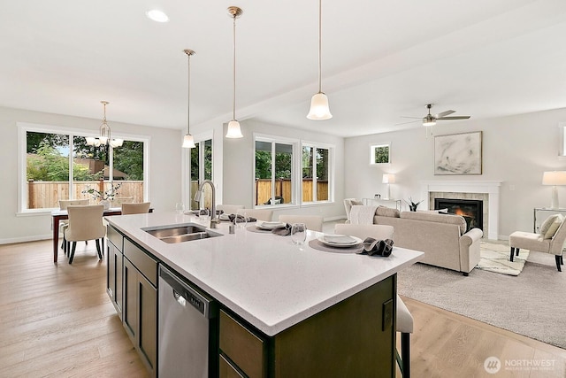 kitchen featuring a tile fireplace, a sink, light wood-style floors, dishwasher, and an island with sink