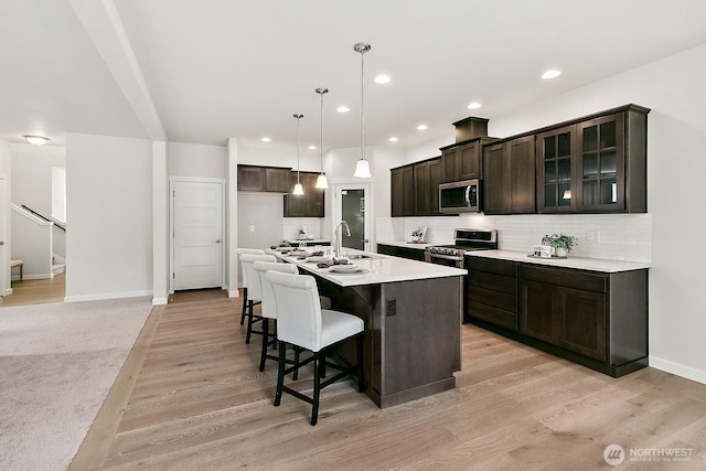 kitchen with stainless steel appliances, light wood finished floors, a kitchen bar, and tasteful backsplash