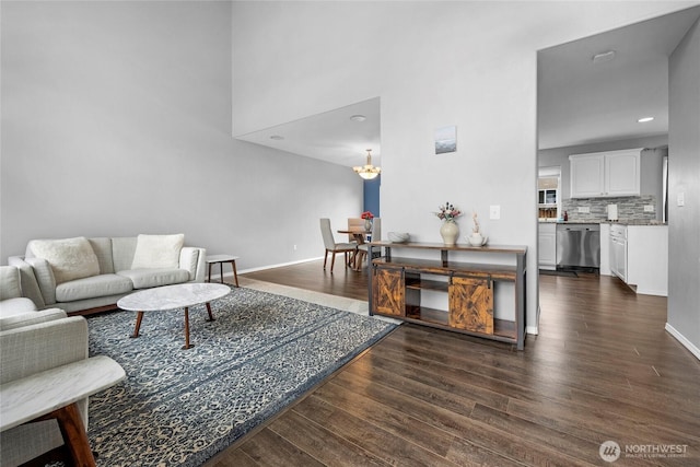 living area with dark wood-style flooring, a towering ceiling, baseboards, and an inviting chandelier