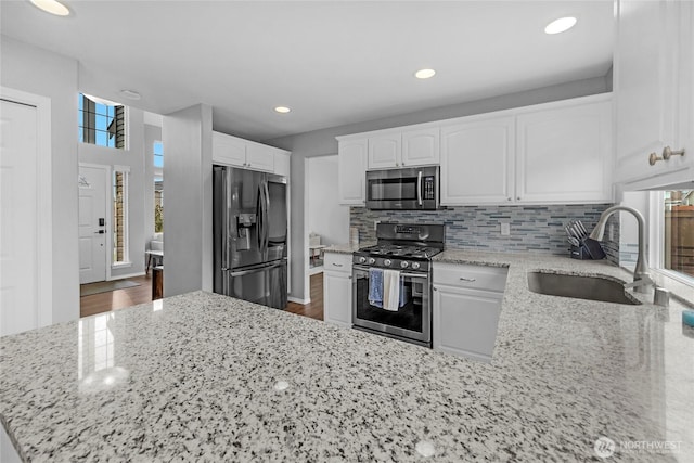 kitchen with light stone counters, stainless steel appliances, backsplash, white cabinetry, and a sink