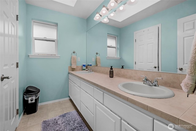 bathroom featuring tile patterned floors, a skylight, a sink, and baseboards