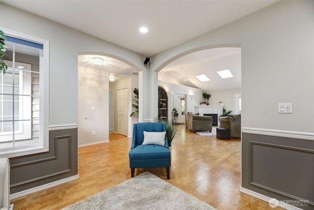 sitting room featuring arched walkways, a fireplace, light wood-type flooring, and lofted ceiling