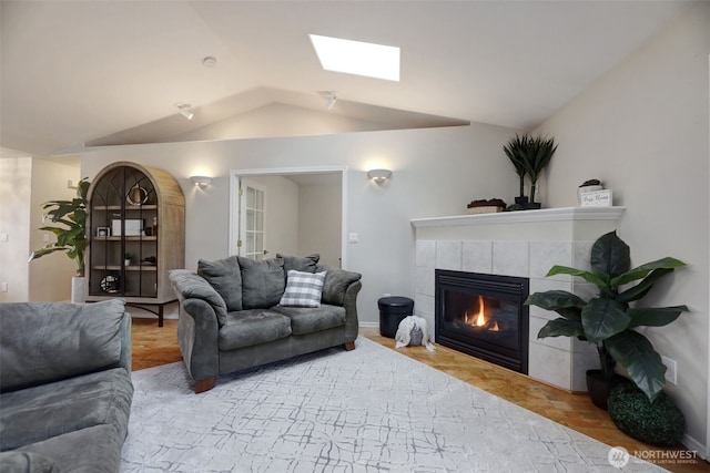 living area with baseboards, vaulted ceiling with skylight, and a tiled fireplace