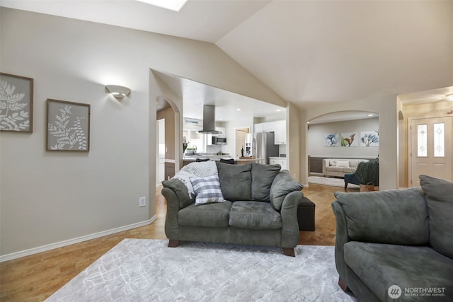 living room with baseboards, arched walkways, light wood-style floors, and vaulted ceiling