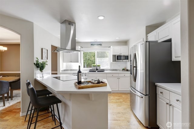 kitchen featuring a breakfast bar, island exhaust hood, arched walkways, appliances with stainless steel finishes, and white cabinets