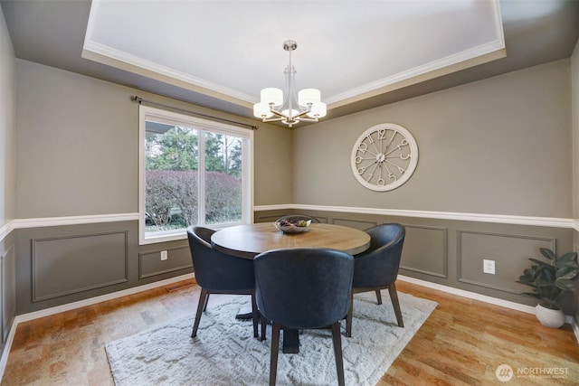 dining area featuring a raised ceiling, a decorative wall, light wood-style floors, and a chandelier