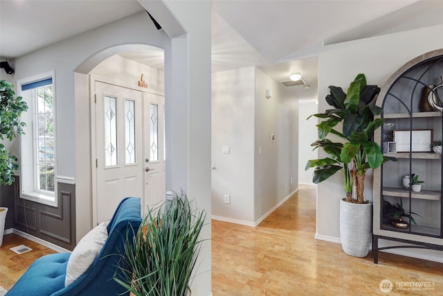 entryway with arched walkways, visible vents, baseboards, and wood finished floors