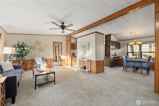 carpeted living room with wooden walls, a wainscoted wall, lofted ceiling with beams, and ceiling fan with notable chandelier