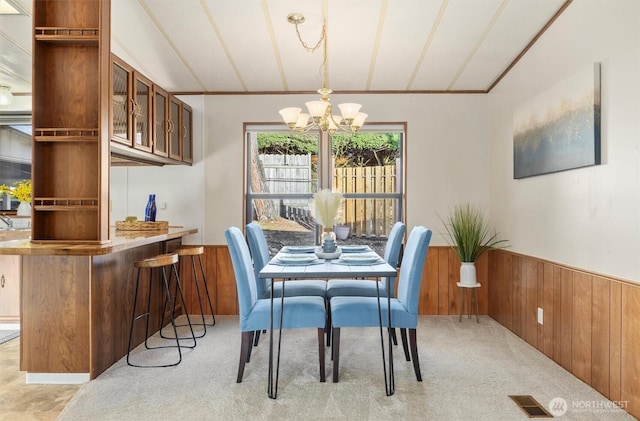 dining area with lofted ceiling, wood walls, visible vents, wainscoting, and an inviting chandelier