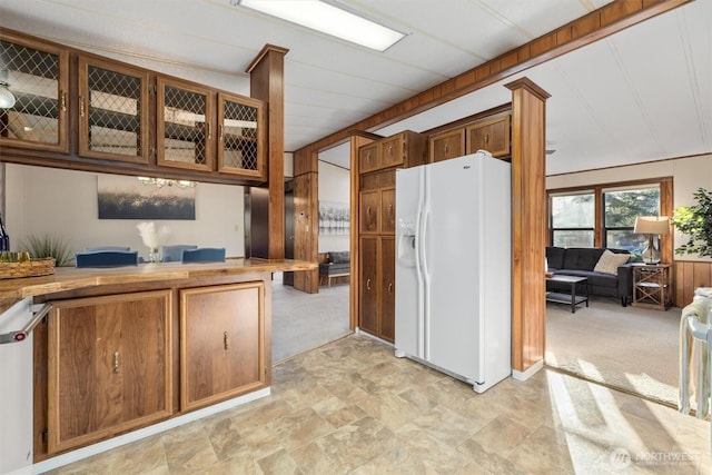 kitchen with light carpet, white refrigerator with ice dispenser, stainless steel dishwasher, brown cabinetry, and glass insert cabinets