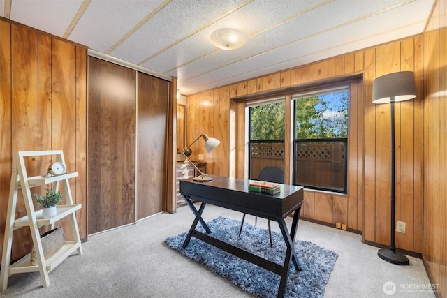 home office featuring a textured ceiling, wood walls, and light colored carpet