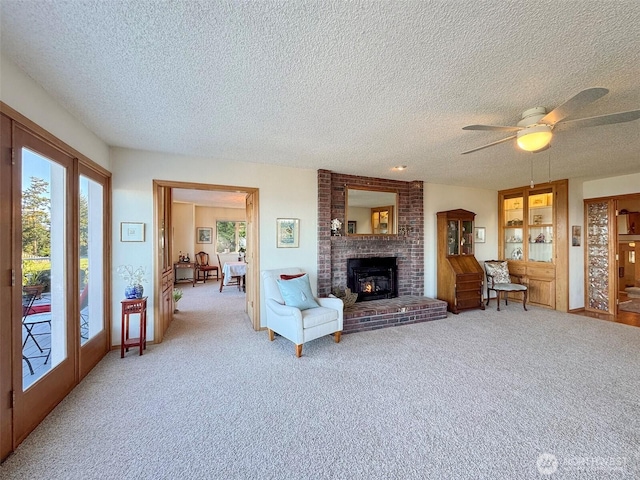 living room with a ceiling fan, a brick fireplace, light carpet, and a textured ceiling