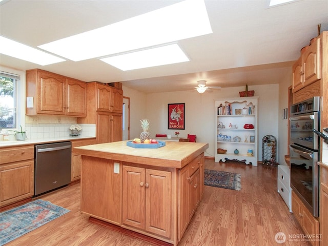 kitchen featuring a kitchen island, light wood-style floors, light countertops, appliances with stainless steel finishes, and decorative backsplash