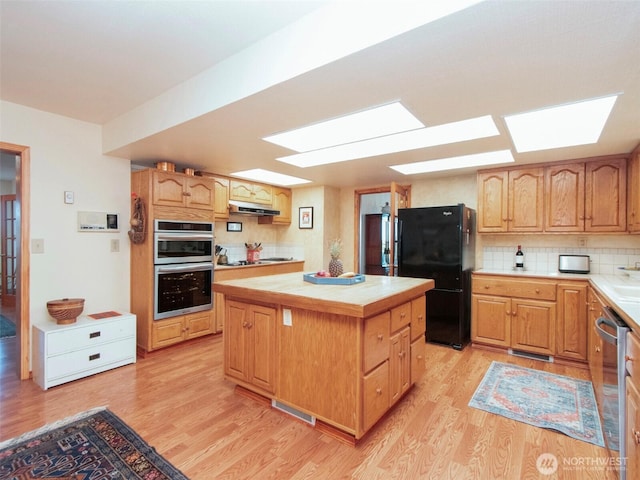 kitchen featuring appliances with stainless steel finishes, decorative backsplash, light wood-style floors, and under cabinet range hood