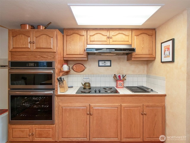 kitchen with tile countertops, tasteful backsplash, stainless steel double oven, under cabinet range hood, and black electric cooktop