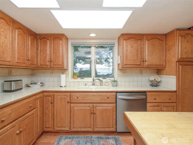 kitchen featuring a sink, stainless steel dishwasher, tile counters, light wood finished floors, and tasteful backsplash