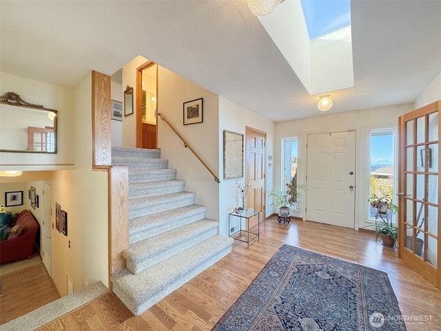 entryway with a skylight, plenty of natural light, stairway, and wood finished floors