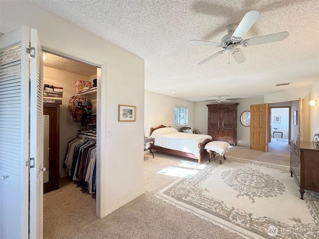 carpeted bedroom featuring a textured ceiling, ceiling fan, visible vents, a spacious closet, and a closet