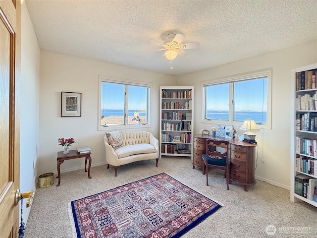 living area with a textured ceiling, carpet flooring, a ceiling fan, and baseboards