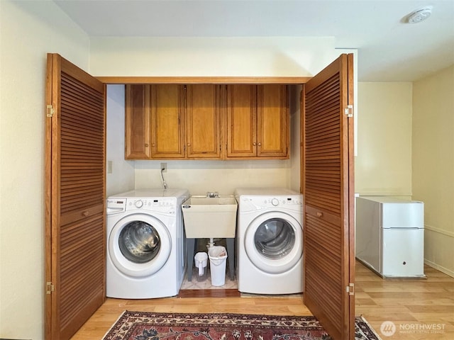 clothes washing area featuring a sink, light wood finished floors, washing machine and clothes dryer, and cabinet space