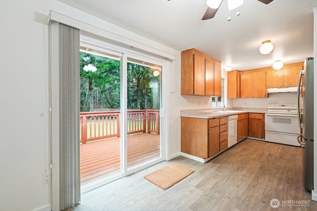 kitchen featuring white appliances, light wood-style floors, light countertops, under cabinet range hood, and a sink