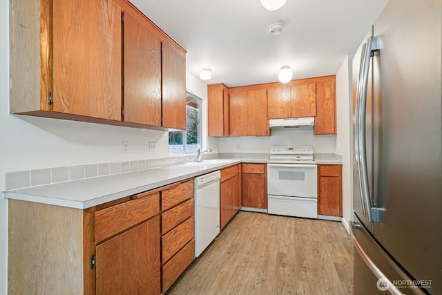 kitchen featuring white appliances, under cabinet range hood, light wood finished floors, and brown cabinetry