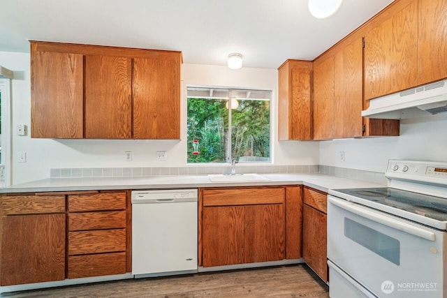 kitchen with brown cabinets, light countertops, a sink, white appliances, and under cabinet range hood