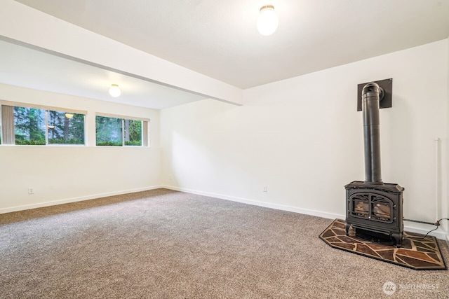 unfurnished living room with beam ceiling, carpet flooring, a wood stove, and baseboards