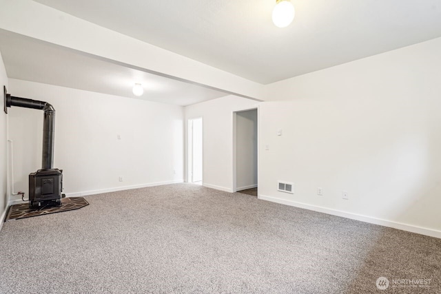 unfurnished living room with a wood stove, carpet flooring, visible vents, and baseboards