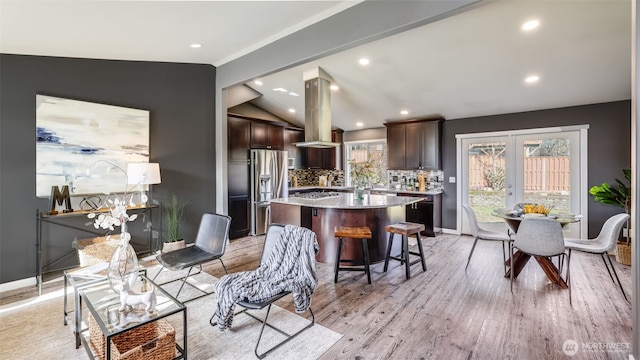 kitchen with island range hood, appliances with stainless steel finishes, a center island, vaulted ceiling, and light wood-type flooring