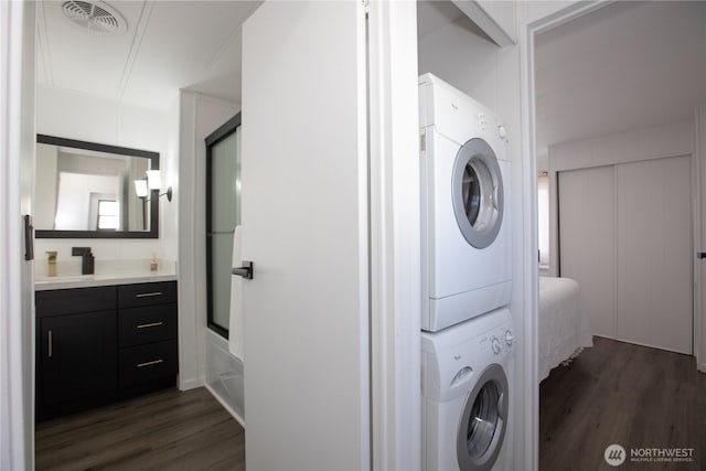 laundry room featuring laundry area, visible vents, dark wood finished floors, and stacked washer and clothes dryer