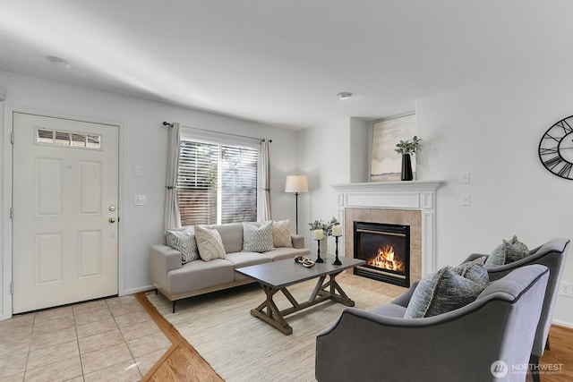 living room with a tiled fireplace, light tile patterned flooring, and baseboards