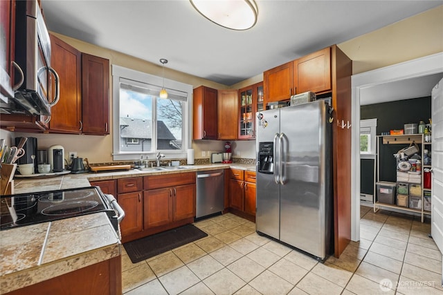 kitchen featuring a sink, appliances with stainless steel finishes, light tile patterned floors, glass insert cabinets, and tile counters