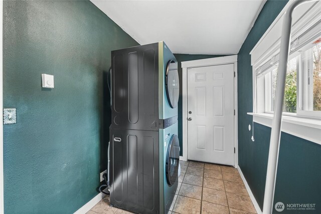 clothes washing area with baseboards, light tile patterned flooring, laundry area, and stacked washer / dryer