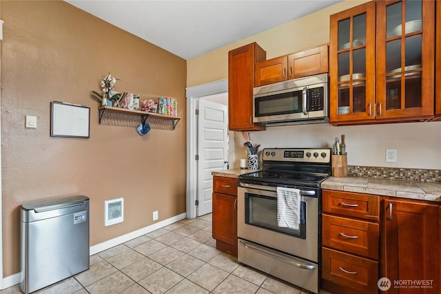 kitchen with baseboards, visible vents, glass insert cabinets, appliances with stainless steel finishes, and brown cabinets