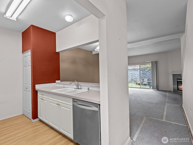 kitchen with light countertops, a fireplace, stainless steel dishwasher, white cabinetry, and a sink