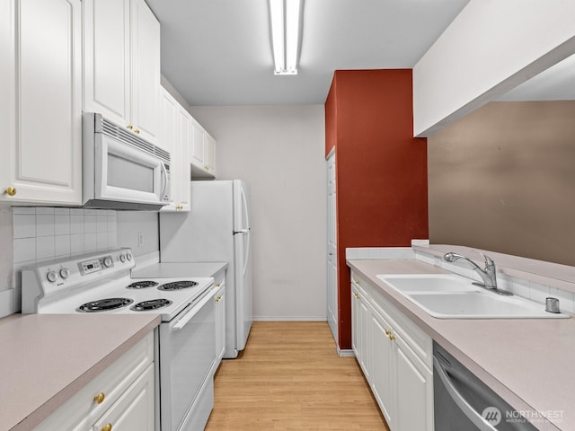 kitchen with white appliances, white cabinetry, light countertops, and a sink