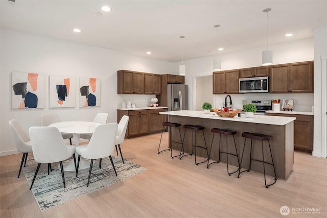 kitchen with appliances with stainless steel finishes, a breakfast bar, light countertops, and light wood-style floors