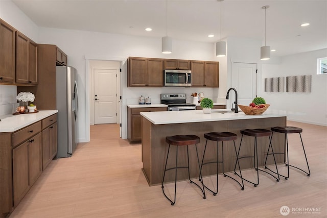 kitchen featuring a kitchen breakfast bar, light wood-style flooring, appliances with stainless steel finishes, and a sink