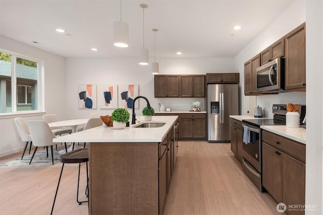 kitchen with a breakfast bar area, stainless steel appliances, light wood-style flooring, and a sink