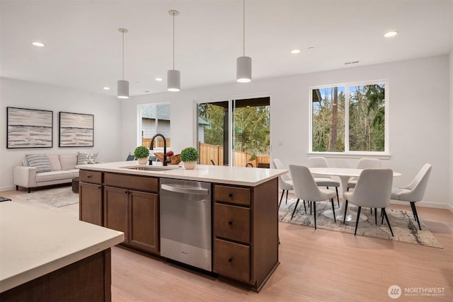 kitchen featuring stainless steel dishwasher, light countertops, pendant lighting, and a sink