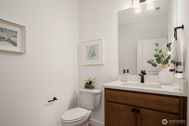 half bath with vanity, toilet, and visible vents