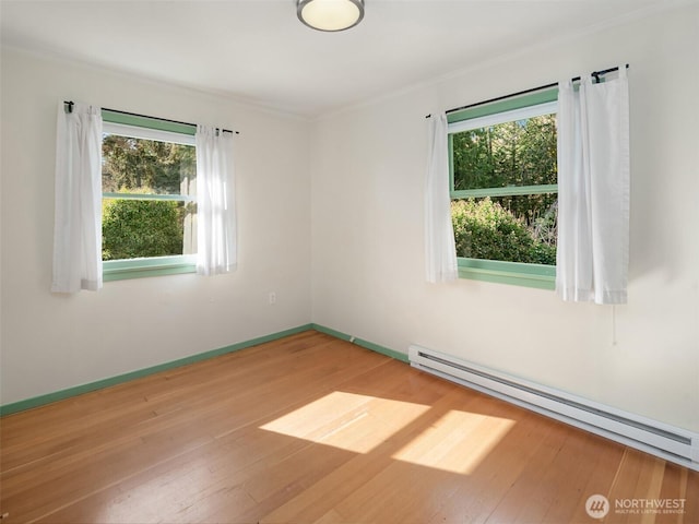 spare room with baseboards, a baseboard radiator, wood-type flooring, and a healthy amount of sunlight