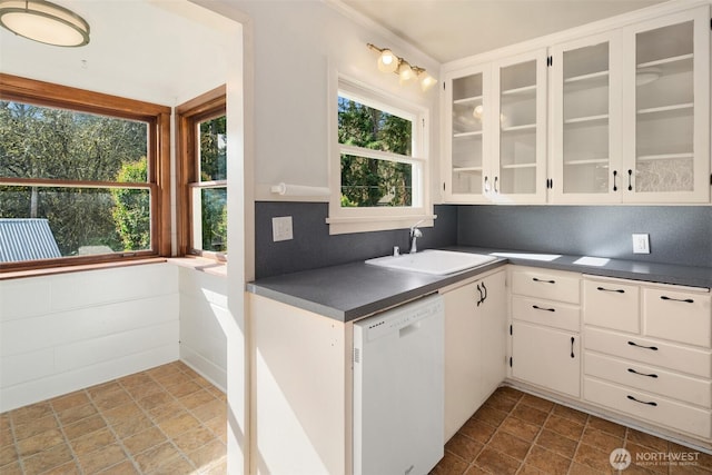 kitchen with dark countertops, white dishwasher, a sink, and white cabinets