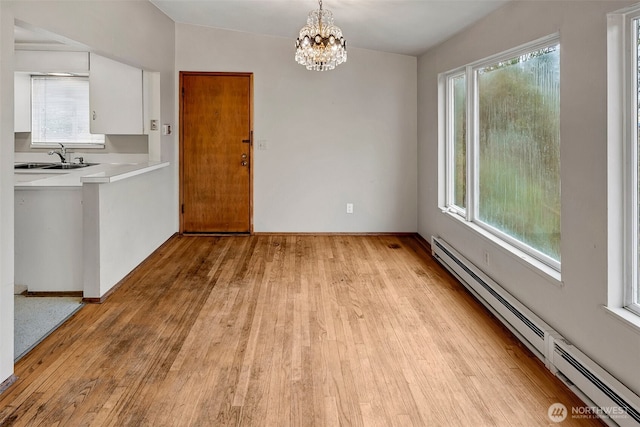 unfurnished dining area featuring a sink, a baseboard radiator, light wood-style floors, and a notable chandelier