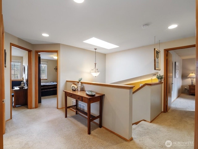 hallway featuring light carpet, an upstairs landing, a skylight, and baseboards