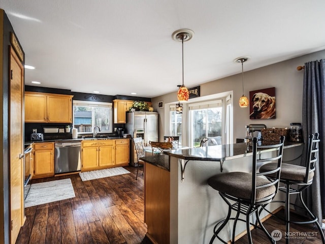 kitchen with a sink, dark countertops, appliances with stainless steel finishes, a breakfast bar area, and dark wood-style flooring